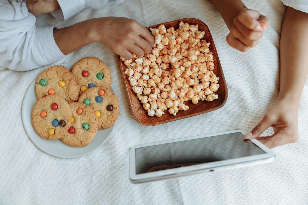 Hands reaching for cookies and popcorn while using a tablet. Perfect cozy indoor setup.